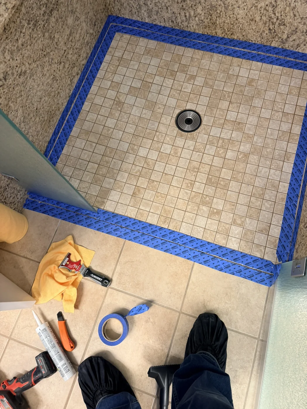 Mosaic shower pan with its perimeter masked in blue tape during preparation
